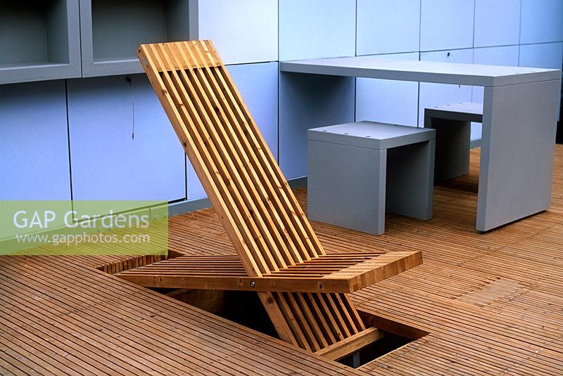 Contemporary styled outdoor deckchair that folds into wooden deck for storage with grey wall stools table
