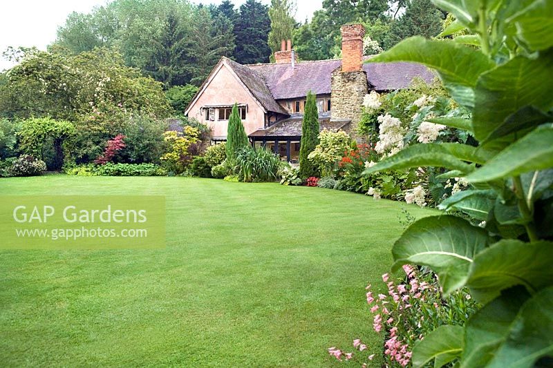 English country cottage garden with large sweep of lawn and mixed borders of shrubs and herbaceous perennials