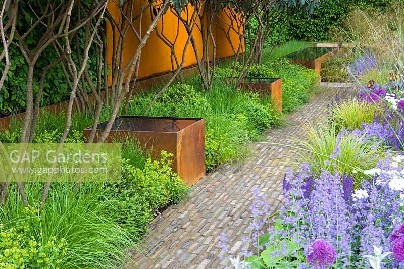Chelsea Flower Show 2006, London, UK. 'The Telegraph Garden' ( des. Tom Stuart-Smith ) brick pathway with metal water containers at edge.