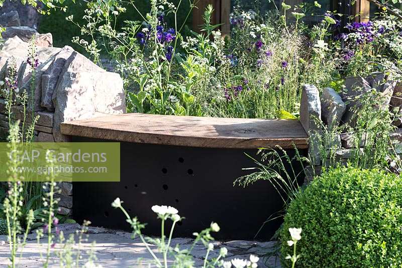 RHS Chelsea Flower Show 2014. 'Vital Earth The Night Sky Garden', designers David and Harry Rich. Simple wooden bench set into rustic wall.  