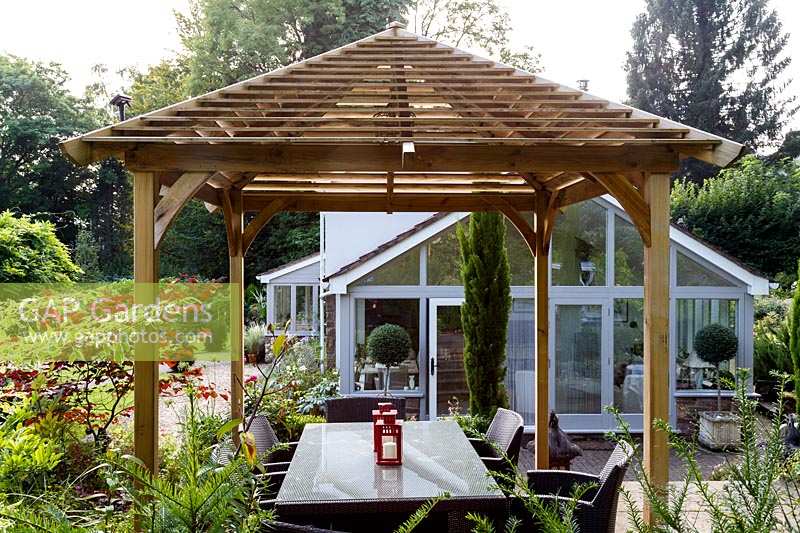 Jackie Healy's garden near Chepstow. Early autumn garden. Japanese style wooden 'pergola' shades dining table in the patio area