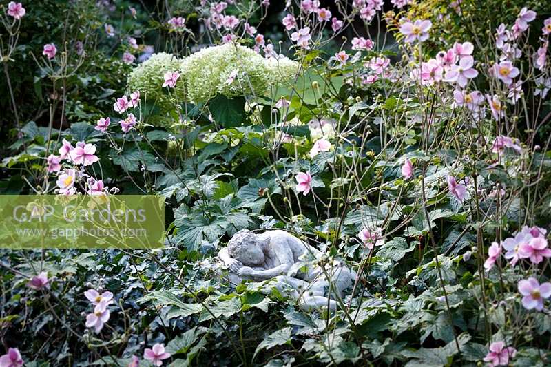 Jackie Healy's garden near Chepstow. Early autumn garden. 'Sleeping' statue amongst Anemone x hupehensis
