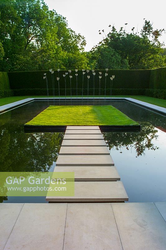 Kiftsgate Court, Gloucestershire, UK, ( Chambers ) Summer. The Water Garden, pond with sculpture designed by Simon Allison. Modern formal design with stainless steel and gilded Bronze, stepping stones