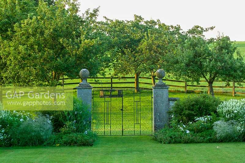 Hodges Barn, Gloucestershire, UK. Summer. view through ornate metal gates into the orchard