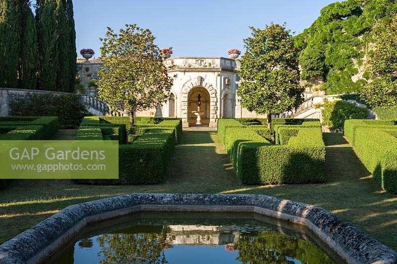 Villa La Foce, Tuscany, Italy. Large garden with topiary clipped Box hedging and views across the Tuscan countryside, pond and Magnolia grandiflora on lower terrace