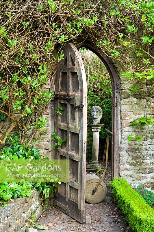 Peter Owen's garden, Watcombe, in Somerset, UK, arched gateway in walled garden with bust on plinth and lawn roller