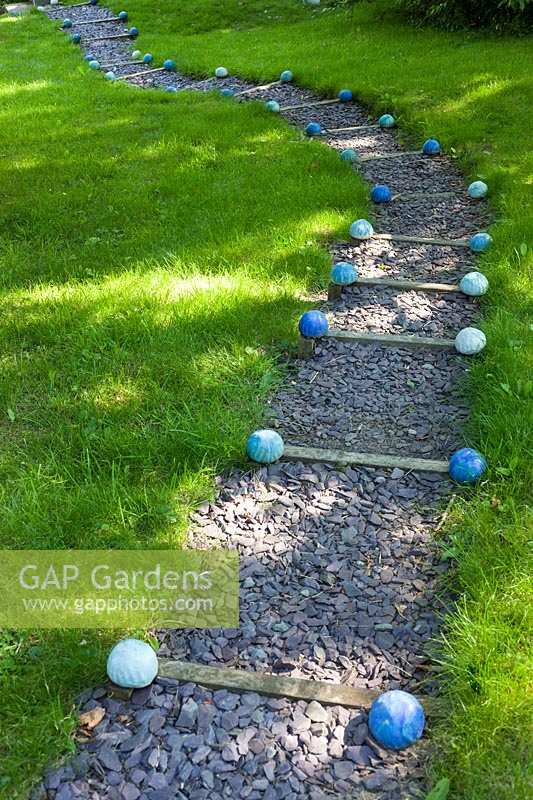 Carole Waller's garden at Bathford, Somerset, summer. Decorative spheres mark the steep path in the garden