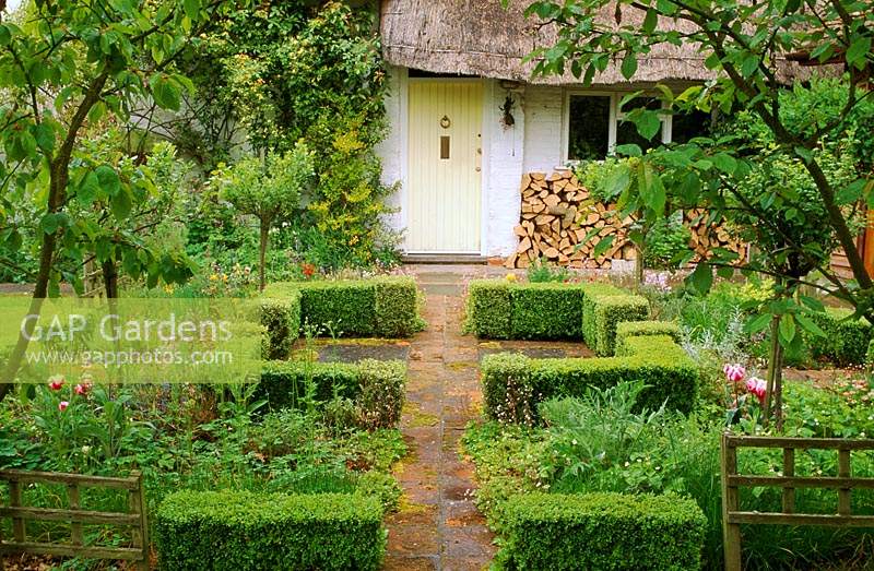 Cottage garden with brick path leading to front door Formal low boxwood hedging