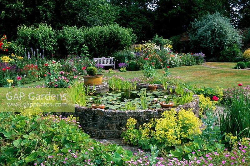 Private garden Sussex Raised circular pond Self seeded perennials in paving Herbaceous border with wooden seat