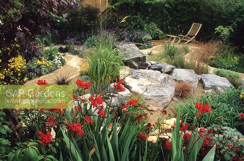 Feng Shui garden Design Pamela Woods red border with Crocosmia Lucifer Rock garden with view through to small deck with lounger