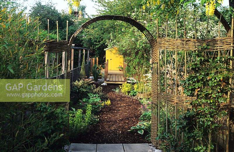 Hallowell Rd London Design Alan Titchmarsh Woven willow fence bark mulched path leading to raised deck and yellow painted shed a