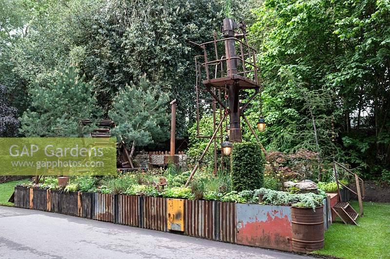 Walker's Forgotten Quarry Garden. Overview of the garden including Taxus baccata - Yew topiary pillars, and orange Geums. Design: Graham Bodle. Sponsor: Walker's Nurseries