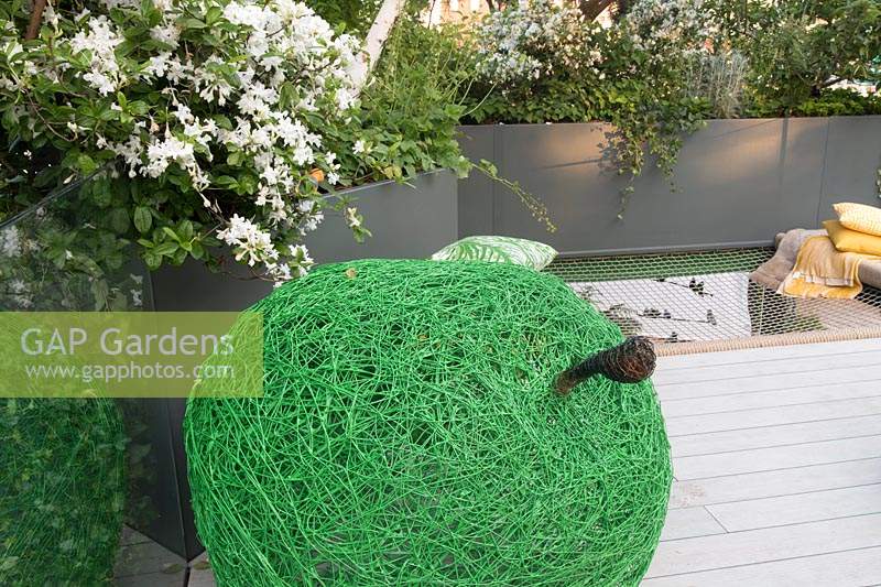 Woven green apple sculpture. The Greenfingers Charity Garden. Designed by Kate Gould Gardens, sponsored by Greenfingers Charity, RHS Chelsea Flower Show, 2019.
