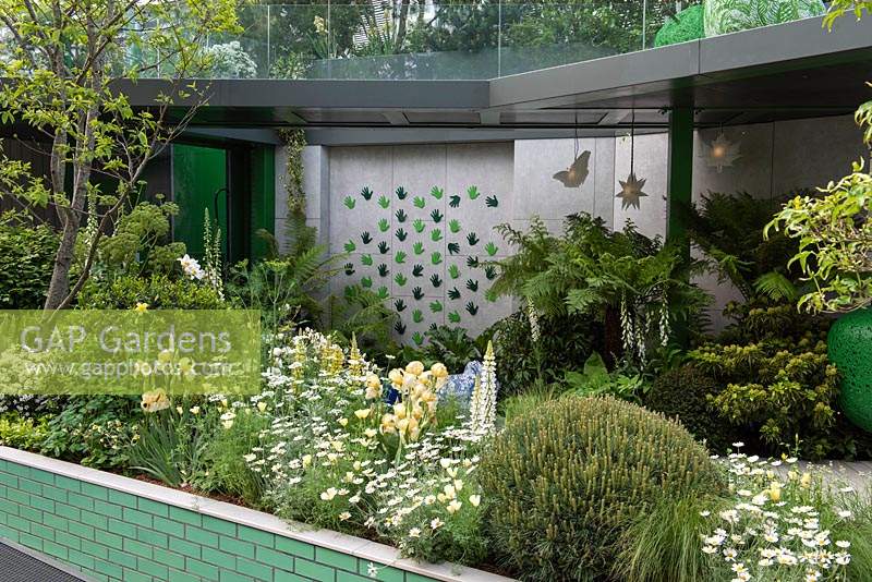 A lush, green, therapeutic space set over two levels, provides an accessible garden and courtyard for people of all ages and abilities. The Greenfingers Charity Garden. Designed by Kate Gould Gardens, sponsored by Greenfingers Charity, RHS Chelsea Flower Show, 2019.