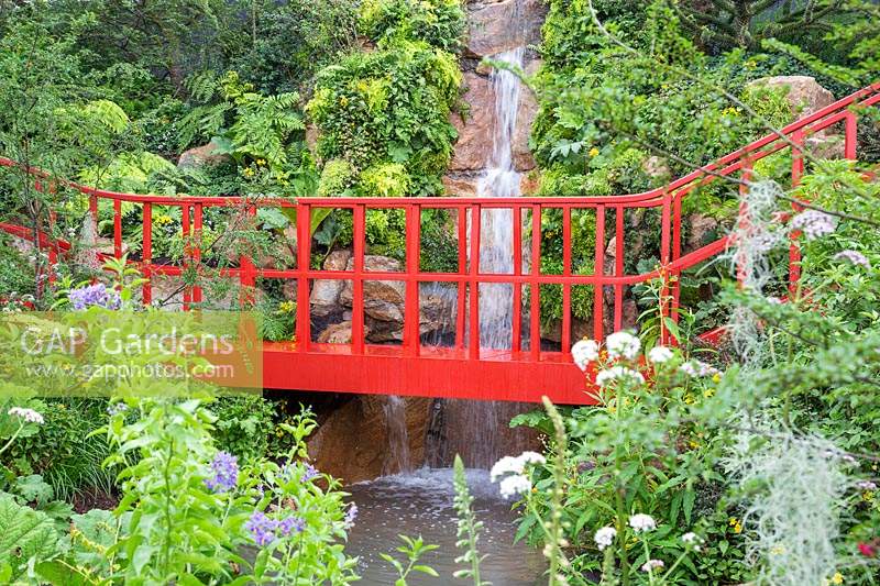 The Trailfinders 'Undiscovered Latin America' Garden at RHS Chelsea Flower Show 2019. View of the bright red brige and water fall over a stream. Design: Jonathan Snow. Sponsor: Trailfinders