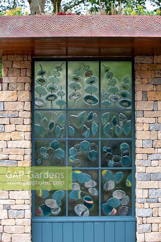 The Warners Distillery Garden, hand crafted glass panel with blue tint created from copper reacting with the glass, inspired by the distillation process, designed by Wendy Newhofer - Design: Helen Elks-Smith - Construction: Bowles and Wyer - Sponsor: Warners Gin. 
