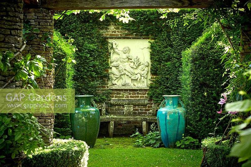 Classic stone seating surrounded by decorative urns and classic sculpture. The Rose Pergola, Highgrove, June, 2019