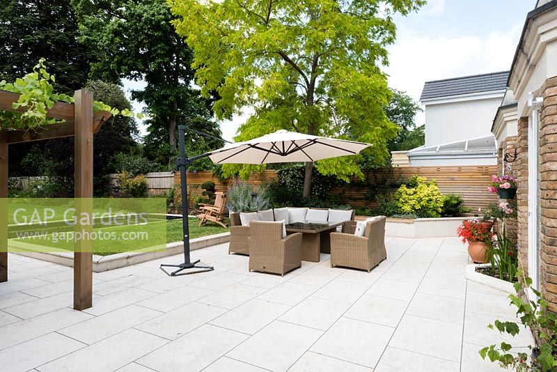 Suburban garden with paved sitting and dining areas. Cedar wood pergola with vine