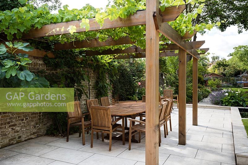 Suburban garden with paved sitting and dining areas. Cedar wood pergola with vine