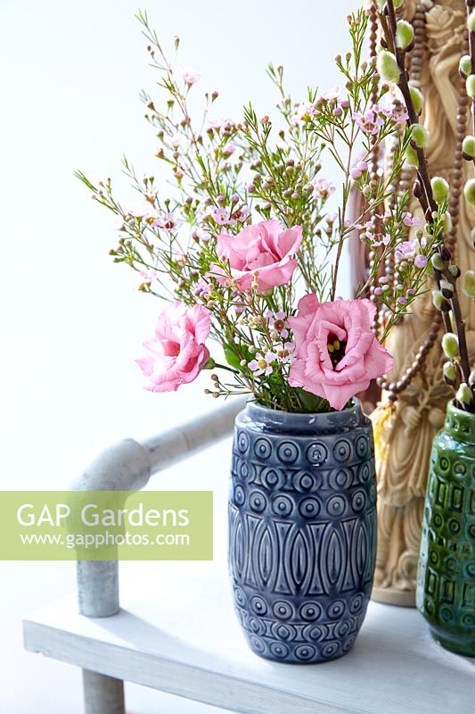 Spring bouquet of Chamelaucium and pink Eustoma in a ceramic vase alongside an ethnic jewellery stand.