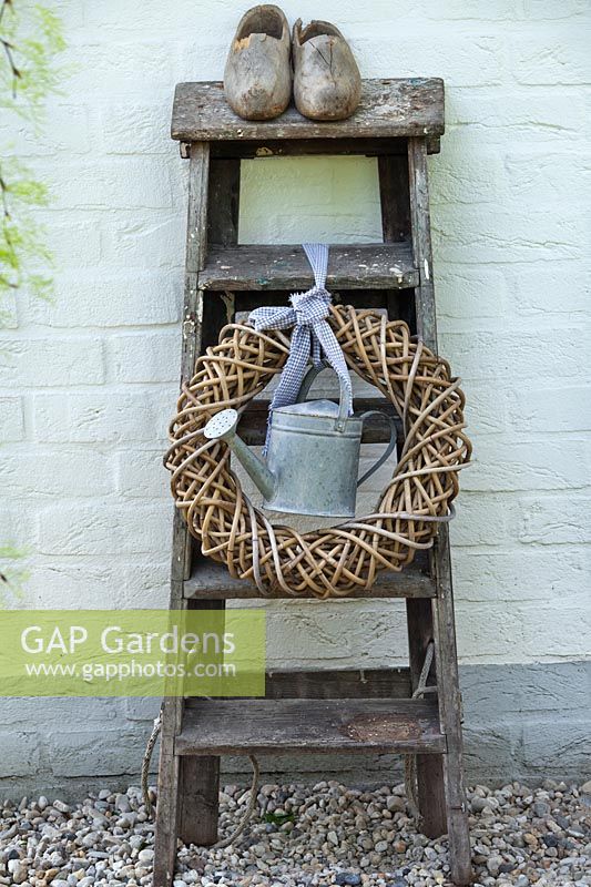 Ladder with wreath, watering can and clogs.