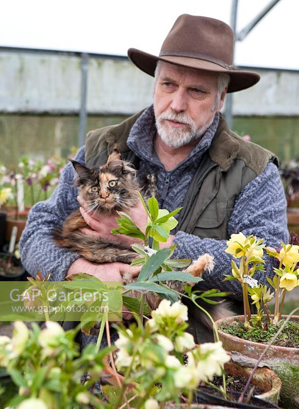 Man holding cat near bench of container-grown plants