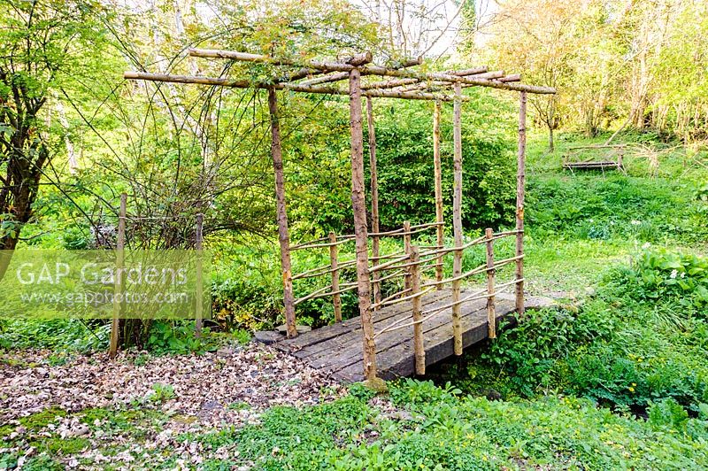 Rustic bridge over stream in the valley garden. Brilley Court Farm, Whitney-on-Wye, Herefordshire