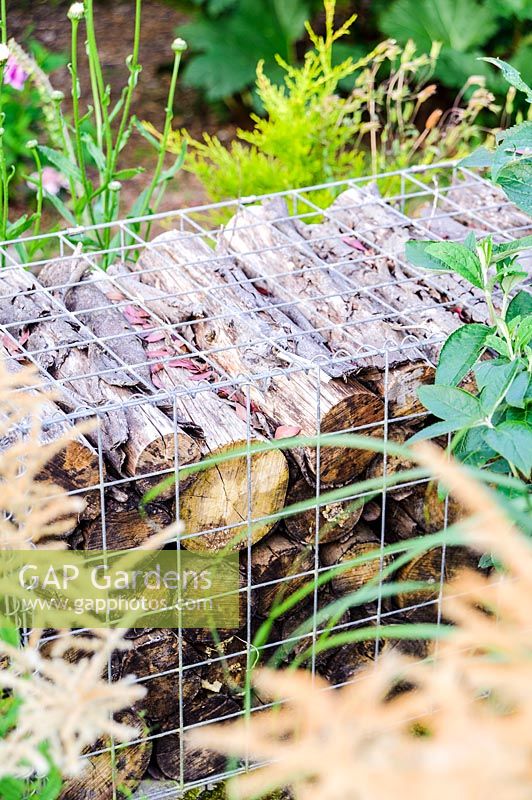 A log filled gabion used to create a low garden wall, Lower Treculliacks Farm, Falmouth, Cornwall, UK.