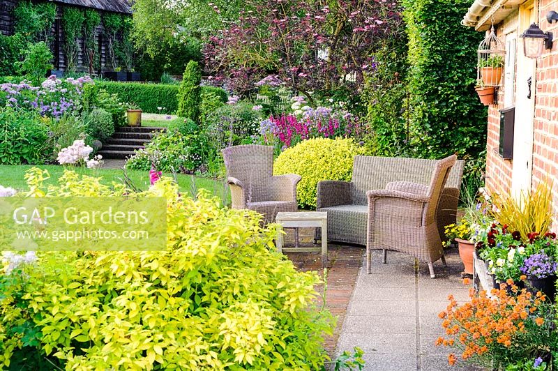 Seating area beside the back door of house, with mixed garden borders beyond, Terstan, Stockbridge, Hants, UK.  