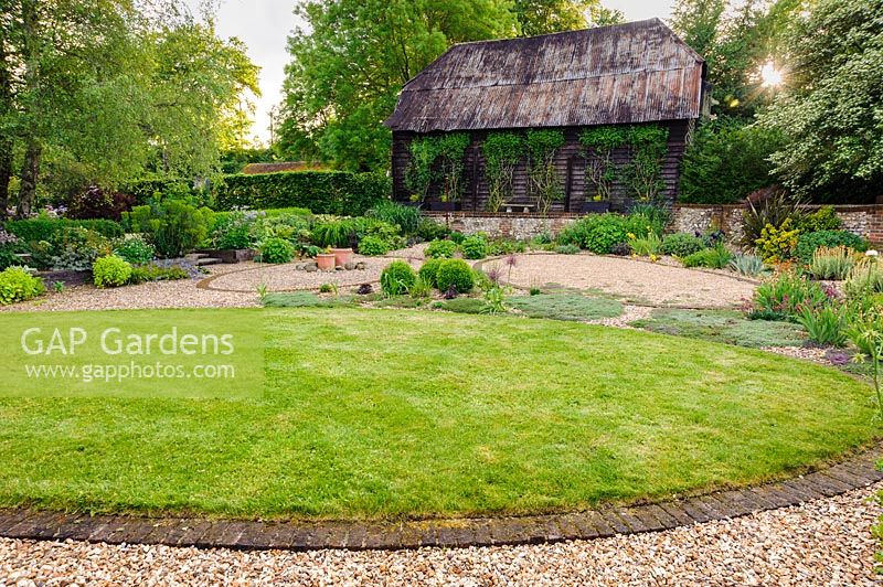 Gravel garden overlooked by black weatherboarded barn, Terstan, Stockbridge, Hants, UK. 