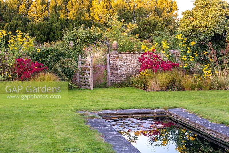 A garden gate opens onto an English country garden with pond. 