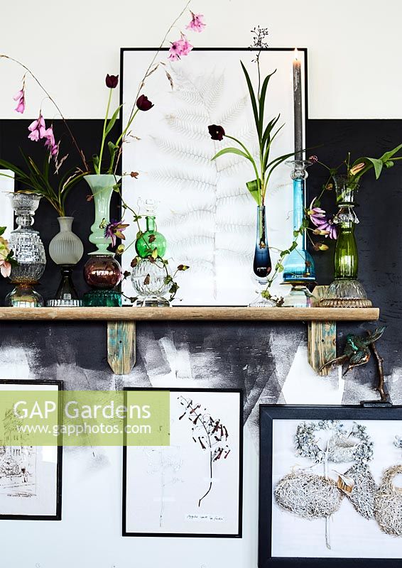 Still life on shelf with multiple vases and framed illustrations.