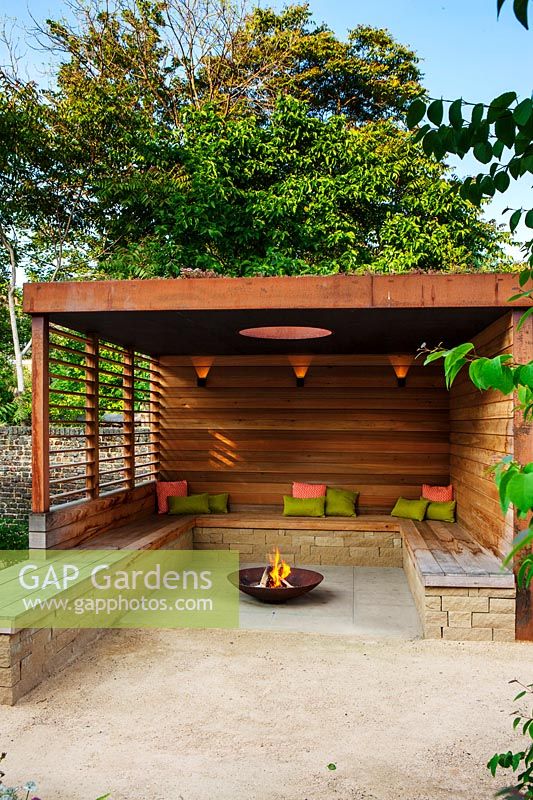  A contemporary pergola with fire pit and wooden bench seating. 
