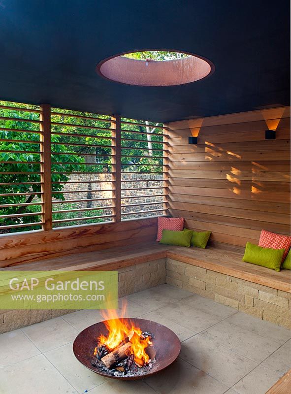 view of a burning fire in a fire pit, surrounded by bench in enclosed seating area.