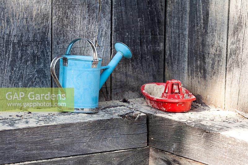 A child's watering-can and a toy boat are left on the edge of the sandpit.