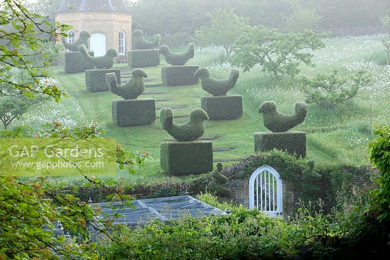 a set of grassed steps bordered by clipped topiary birds lead up to stone dovecot.
