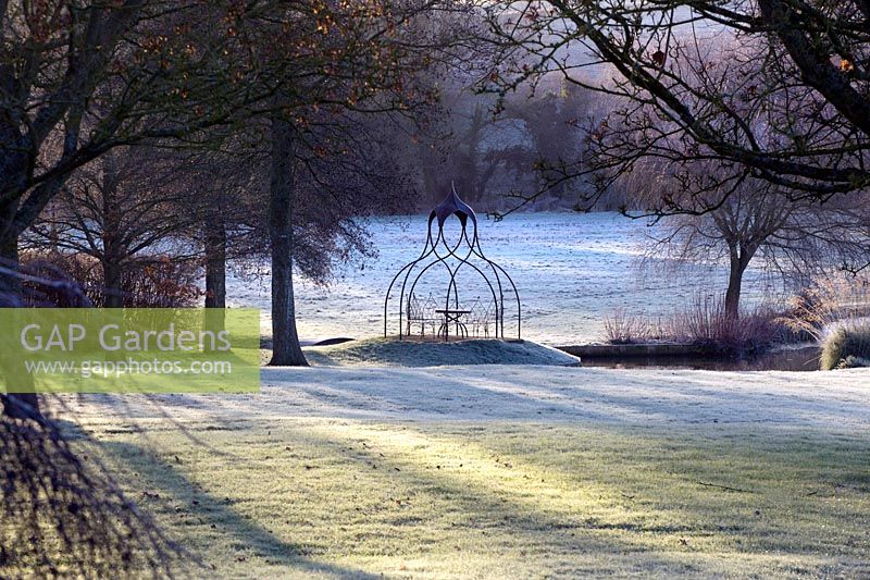 View across frosty lawn to metal table and pergola and fields beyond. 