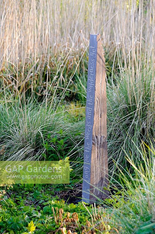 Slate stone inscribed with 'Long the weeds and the wilderness yet' with grasses in wild garden.
