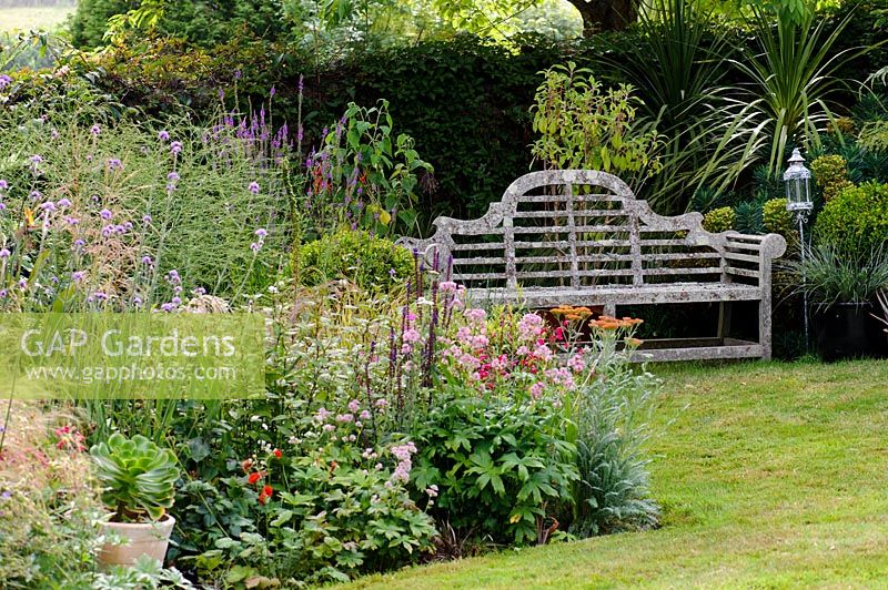 A wooden bench looks over a flowering perennial border. 