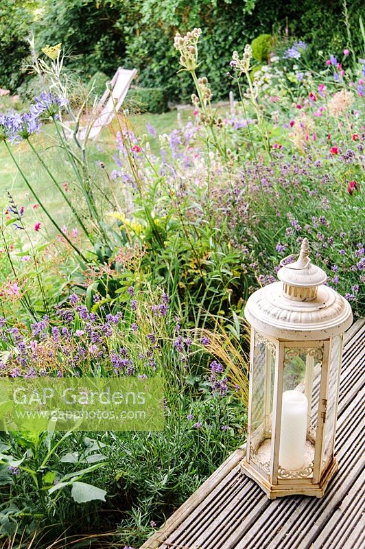 Candle lantern on the decking, overlooking flowering border. 