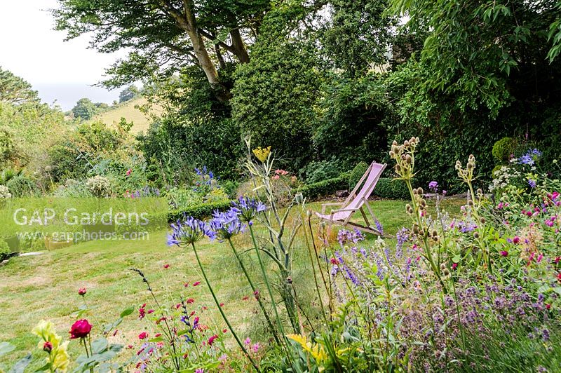 View over flowering perennial border to deckchair on the lawn. 