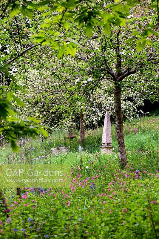 View up flower-filled grass slopes of orchard to stone Obelisk.