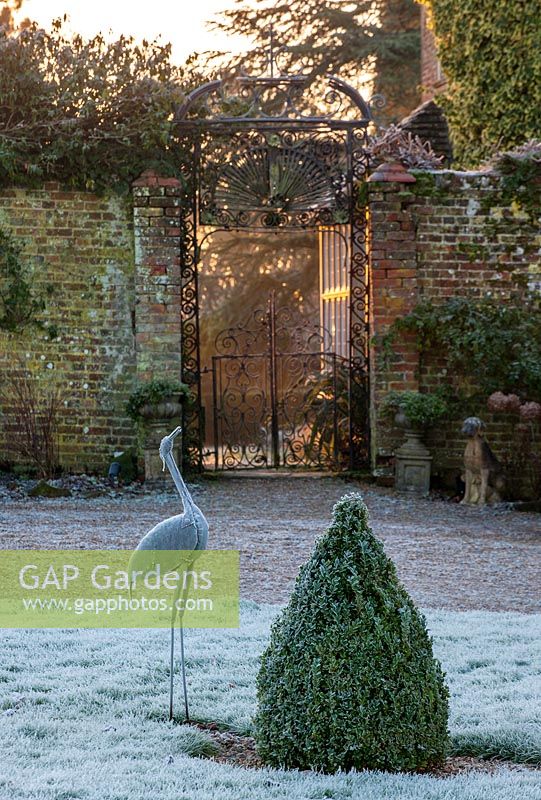Cast iron gate with frosted metal bird sculpture and box topiary, West Sussex