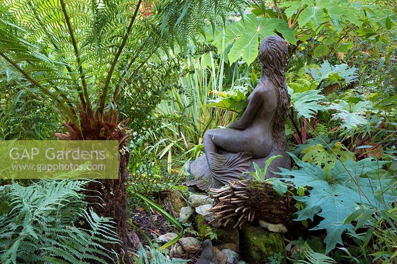 Statue of mermaid surrounded by bold foliage. 