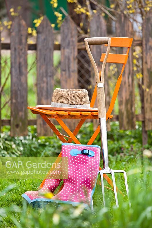 Digging fork and boots resting against seat with hat in a garden setting