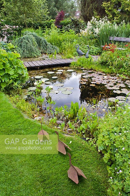 Pond area with borders, and ornamental metal ducks with wooden decking path. 