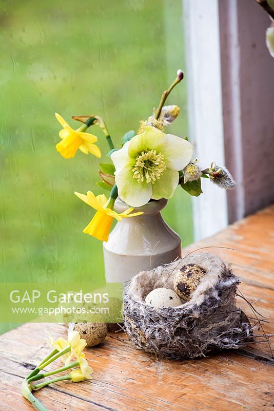Small spring posy in earthenware bottle with birds nest and eggs. 