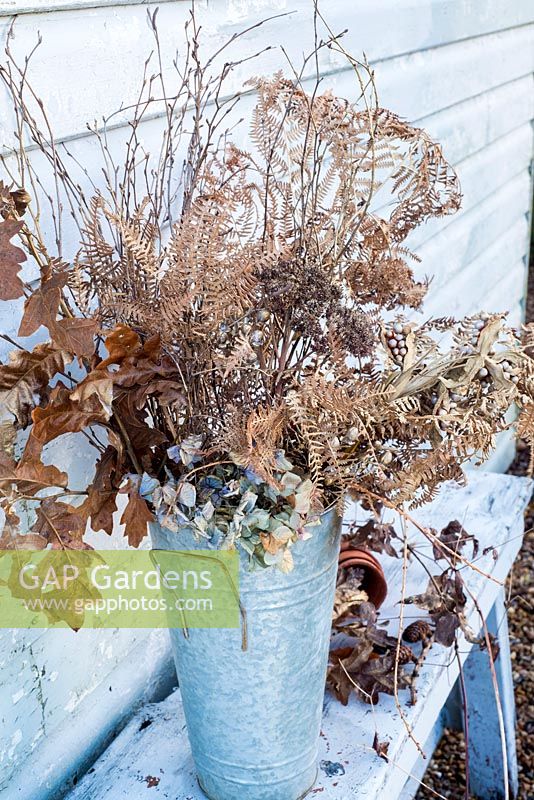 Selection of sprayed gold dried seedheads, ferns, berries and leaves displayed in florist's bucket