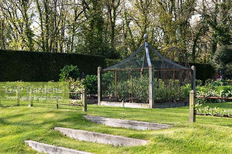 Sleeper steps lead up to a formal kitchen garden with ornate fruit cage