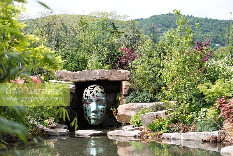 'Leaf Spirit' sculpture by Simon Gudgeon, overlooking pond in 'The Spirit of the Woods' garden, RHS Malvern Spring Festival, 2018. 